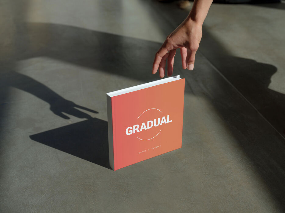 Mockup of a square book on a concrete surface with a hand reaching (Mockuuups Studio).jpg